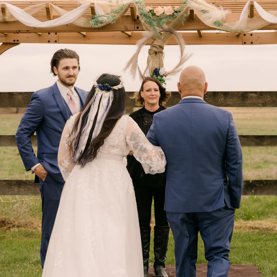 Reverend Stacey Miles leading a wedding ceremony beneath a decorated wooden arbor